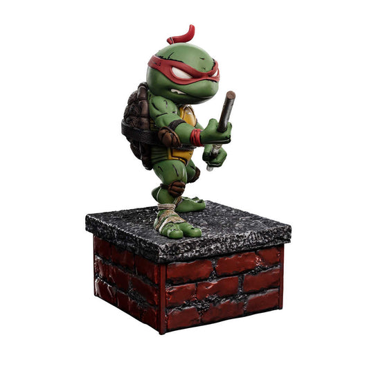 Raphael Teenage Mutant Ninja Turtle figure stands on a brick and concrete-looking base, holding sai sticks.